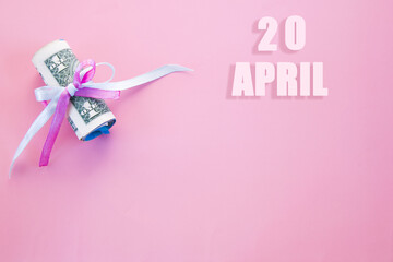 calendar date on pink background with rolled up dollar bills pinned by pink and blue ribbon with copy space. April 20 is the twentieth day of the month