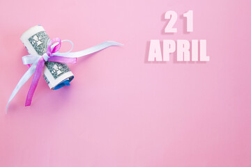 calendar date on pink background with rolled up dollar bills pinned by pink and blue ribbon with copy space. April 21 is the twenty first day of the month