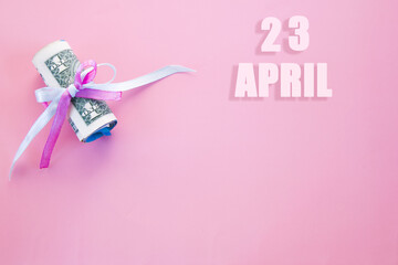 calendar date on pink background with rolled up dollar bills pinned by pink and blue ribbon with copy space. April 23 is the twenty-third  day of the month