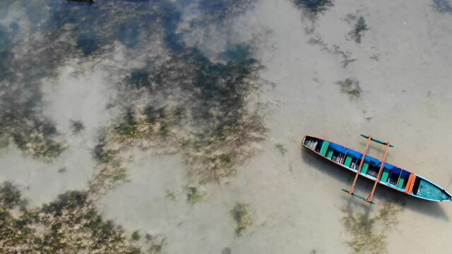 Local fishing boat sits empty in shallow water off Saint-Marie, Madagascar. Aerial view travelling overhead.