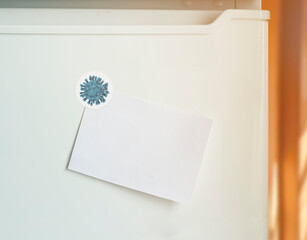 Empty note and magnet with Coronavirus on refrigerator door in kitchen. Space for text