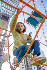 Cute European Beautiful natural teenage girl looks through the rope web on playground.