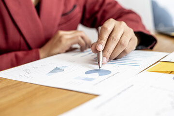 Business Woman holding a pen pointing to a pie chart on the monthly sales paper, she is examining the company's sales data after the sales department has made a summary. Sales management concept.