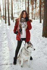 Cute girl in a winter park. A woman plays with a dog. Girl in a red jacket with a hood plays with a husky