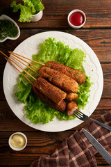 Tasty corn dog with sauce and salad served on white plate