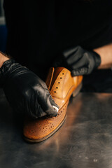 Close-up hands of shoemaker wearing black latex gloves rubbing old light brown leather shoes for...
