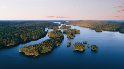 Aerial view of small islands on a blue lake at sunset. Birds eye view of scenic lake surrounded by green forest.