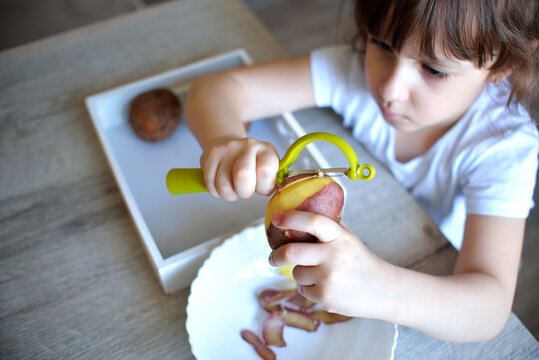 Child Peels Potatoes With A Green Peeler. Preschooler Prepares Food. Montessori Materials For A Lesson From The Practical Life Zone.