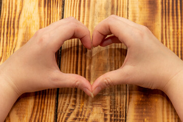 Women's hands in the shape of a heart. Wood background