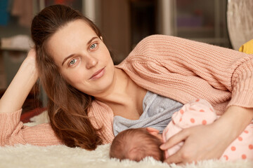 Breastfeeding for newborns, helpful tips for feeding baby, love and tenderness, dark haired happy female lying in bed with her infant, looks smiling at camera.