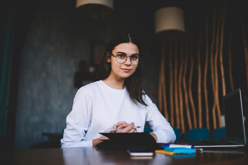 Confident young woman working on laptop and taking note in planner