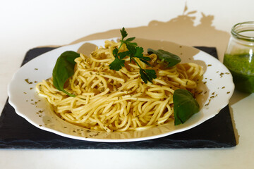 Tasty Spaghetti with basil and parsley leaves in a plate and a glass of pesto Sauce