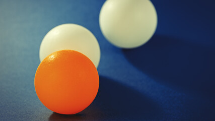 One orange ball and two white balls lie on a blue surface.