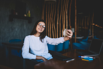 Cheerful student taking selfie on mobile phone in cafe