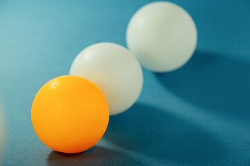 One orange ball and two white balls lie on a blue surface.
