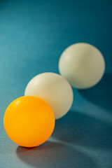 One orange ball and two white balls lie on a blue surface.