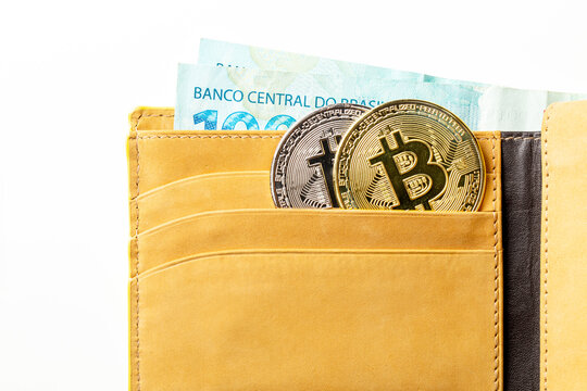 Carteira de couro com criptomoedas Bitcoin e c&eacute;dulas de dinheiro isolada em fundo branco. Notas de cem Reais brasileiros.