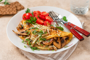 Omelet with mushrooms close-up. Tasty breakfast or lunch. Omelet with champignons, cheese, and tomatoes in a white plate on the table. 