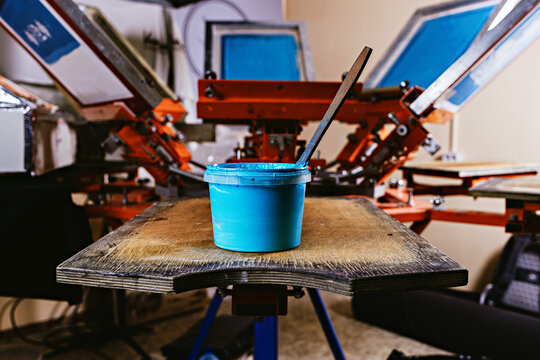 selective focus photo of can of blue paint on wooden shelve on the print screening apparatus. serigraphy production. printing images on t-shirts by silkscreen method in a design studio