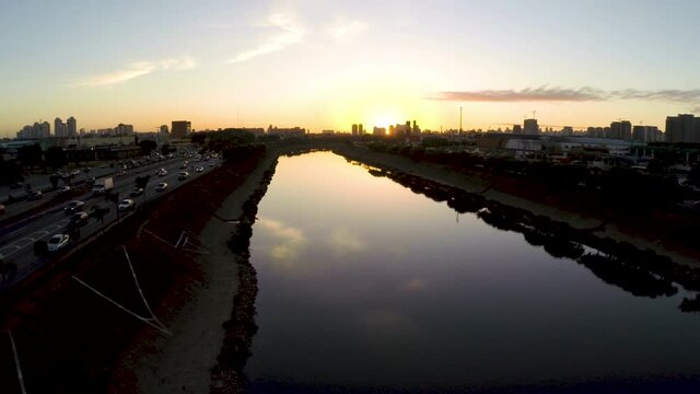 Cinematic aerial sunset shot rising above the modern city of Sao Paulo, Tiete River and highways in the foreground.