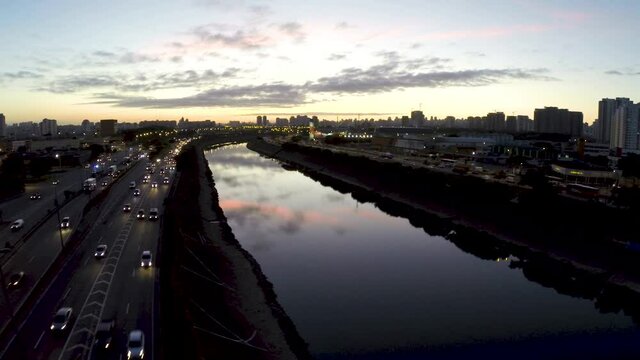 Rush hour traffic on the highways next to the Tiete River in Sao Paulo, Brazil. Aerial drone shot over the river at sunset.