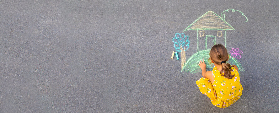 The child draws a house on the asphalt. Selective focus.