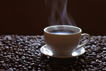 A cup of hot coffee from which steam comes out, surrounded by coffee beans.