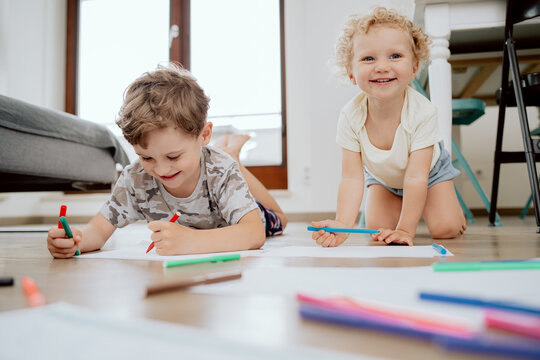 Little boy and girl draw together in white room with window. Kids doing homework, drawing. Children paint pencils. Art and crafts for toddler and preschooler