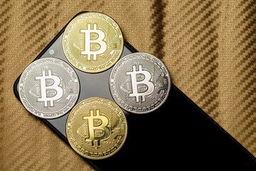 Moedas de bitcoin douradas e prateadas em cima de aparelho celular desligado. Quatro tokens de criptomoedas com fundo dourado desfocado.