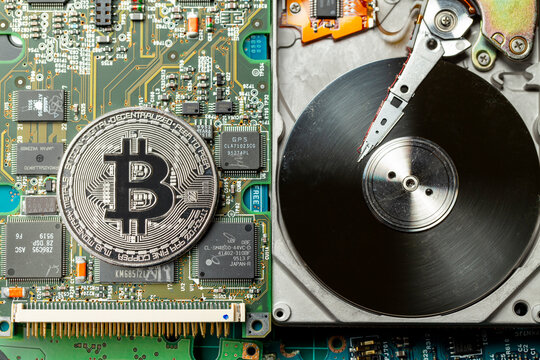 Token de criptomoeda Bitcoin prateada em cima de placas eletr&ocirc;nicas e pe&ccedil;as de computador com um disco r&iacute;gido aberto. Visto de cima.