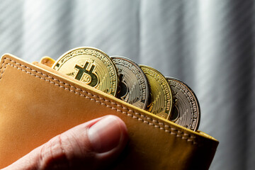 Mão segurando carteira cheia de tokens de Bitcoins. Criptomoedas ouro e prata com fundo desfocado. - obrazy, fototapety, plakaty