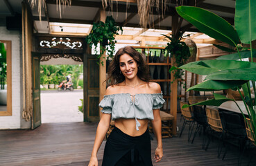 Happy ethnic woman in trendy outfit standing in cafe