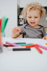 Portrait of smiling pre-school girl sitting at her kitchen table playing with plasticine. The cute lovely girl is spending his afternoon free time at home.