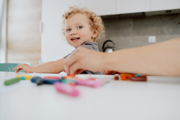 Portrait of smiling pre-school girl sitting at her kitchen table playing with plasticine. The cute lovely girl is spending his afternoon free time at home.