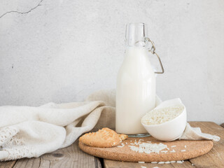 Vegan rice  milk and bowl with a rice  .Non dairy , alternative milk. Healthy vegetarian food and drink concept. Copy space . A bottle of rice milk and raw rice on a wooden table  and a napkin