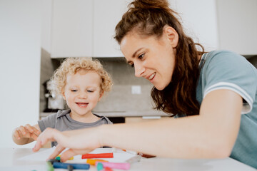 A beautiful mother sits at the kitchen table with her preschool-aged daughter and makes something out of plasticine. Mom is spending her afternoon free time with her daughter.