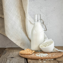 Vegan rice  milk and bowl with a rice  .Non dairy , alternative milk. Healthy vegetarian food and drink concept. Copy space . A bottle of rice milk and raw rice on a wooden table  and a napkin