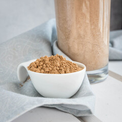 Guarana powder in a white boul and guarana energy milk shake on a white  wooden table and grey napkin . Super foods .