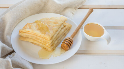 Pancakes  , honey and wooden honey spoon on a white plate . Pancakes on a white wooden table .   Russian blinis and honey with a copy space . 