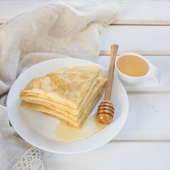 Pancakes  , honey and wooden honey spoon on a white plate . Pancakes on a white wooden table .  ...