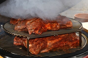 A large beef steak that makes smoke being cooked in the grill of an outdoor barbecue