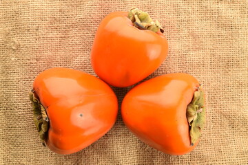 Three juicy ripe persimmons on sacking, close-up, top view.