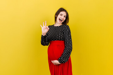 positive pregnant woman showing okay gesture against her belly at colored background. Easy and happy pregnancy. Copy space