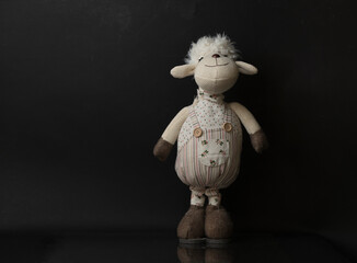 samotna owieczka maskotka na czarny tle z delikatnym odbiciem - obrazy, fototapety, plakaty