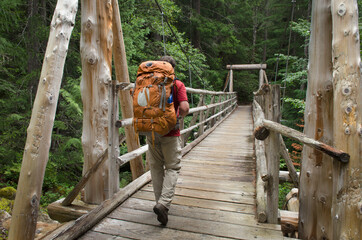 USA, Washington State. Backpacker on suspension bridge over Canyon Creek, Suiattle River Trail, Glacier Peak Wilderness North Cascades.
