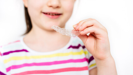 Little girl is holding invisible aligner orthodontic and braces. Close-up, banner, copy space