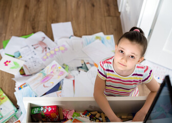 A preschool girl tidies up the dresser in her room. A child among a mess of a heap of papers,...