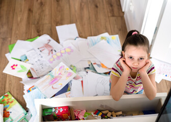 A preschool girl tidies up the dresser in her room. A child among a mess of a heap of papers,...