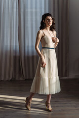 Fototapeta premium Cute young girl stands in the studio on the background of curtains. Stylish fashionable designer clothes.
