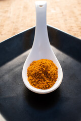 turmeric in a white ceramic spoon on a black plate, cork background